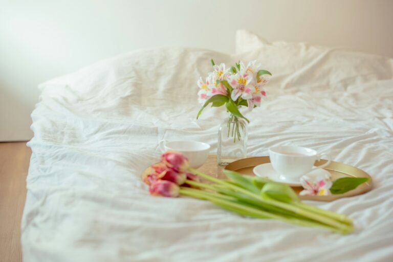 a vase of flowers and two cups on a bed