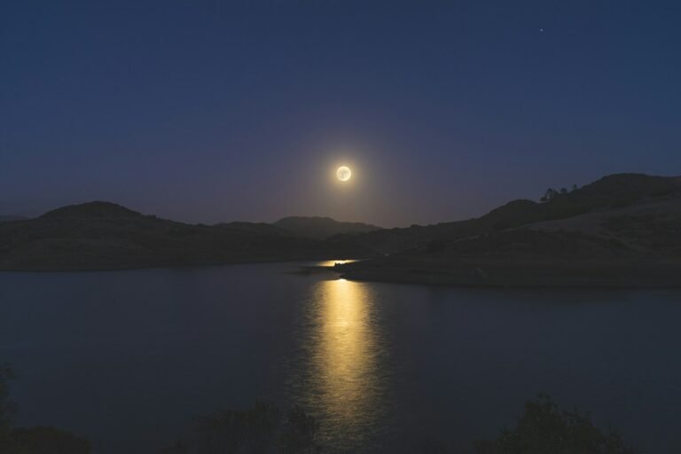 a full moon rising over a lake with mountains in the background